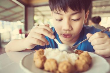 Asya sevimli çocuk yemek kahvaltı ve kamera ile gülümsemek yüz arıyorum 