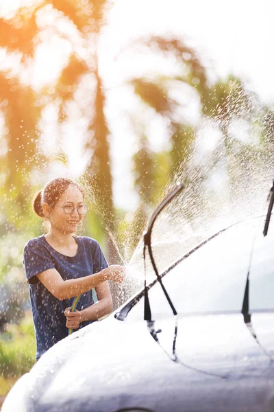 Junge asiatische Frau Wasser sprühen ihr Auto mit Wasserschlauch waschen es — Stockfoto