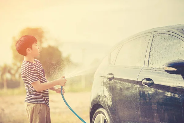 Junge asiatische süße junge Wasser Spray sein Auto mit Wasser Rohr Waschen — Stockfoto