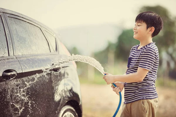 Junge asiatische Kind Wasser sprühen sein Auto mit Wasserschlauch wäscht es — Stockfoto