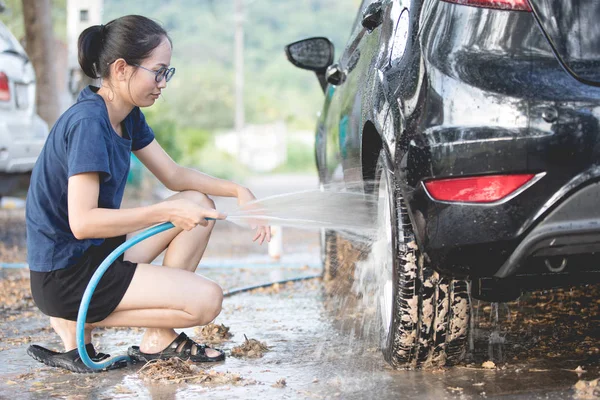 Junge asiatische Frau Wasser sprühen ihr Auto mit Wasserschlauch waschen es — Stockfoto