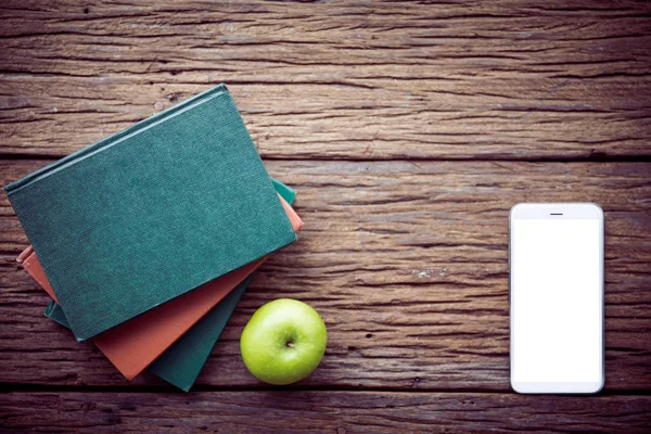 Green apple , books with cell phone on wooden background.