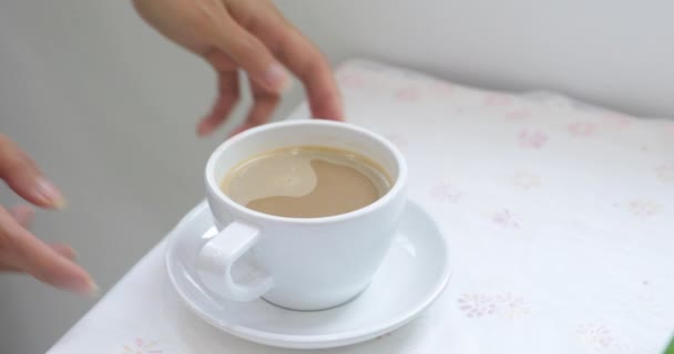 女性手特写从桌子上拿着热咖啡的白杯子 然后照相机用杯子向上移动 这个女人开始喝她的咖啡 — 图库视频影像