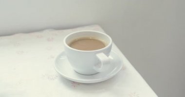 Beyaz bir fincan sıcak kahve tablo ile alarak eller closeup görünümü. Daha sonra kamera ile bir fincan yukarı taşır ve bu kadın onu kahve içmeye başlar.