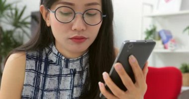 Asyalı kadın evde akıllı telefon kısa mesaj yazarak. Bir masada oturan ve cep telefonuyla genç kadın Resim kırpılmış.
