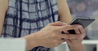 Asyalı kadın evde akıllı telefon kısa mesaj yazarak. Bir masada oturan ve cep telefonuyla genç kadın Resim kırpılmış.