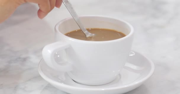 一杯咖啡 年轻的亚洲白人妇女用手将咖啡与金属勺子混合在白色大理石桌上的白色陶瓷杯中 — 图库视频影像