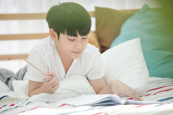Asian söt liten pojke läser bok med leende ansikte . — Stockfoto