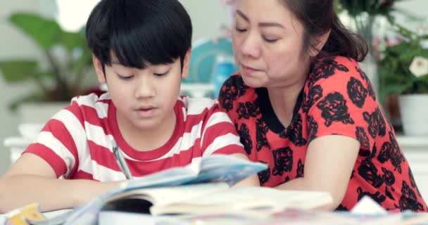 认真的亚洲母亲和儿子在起居室做作业 妈妈教儿子如何才能天才 — 图库视频影像