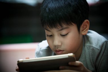 Asyalı çocuk yalan ve oynarken oyun üzerinde dijital Tablet evde