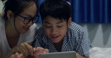 Asya ailesi genç anne oğluyla bir cep telefonu veya bir yatakta smartphone ile oynamak. gece