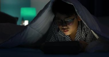 Genç çocuk bir cep telefonu veya bir yatakta smartphone ile oynamak. gece