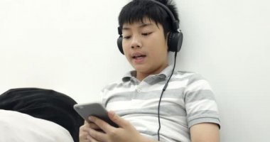 Akıllı telefon ve kulaklık ile uyanık yalan ve evde müzik bir mutlu Asya varoluş çocuk portresi. Çocuklar, dinlenme ve teknoloji kavramı