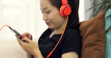 Yaşam tarzı müzik kulaklık için dinleme ve evde kanepede smartphone kullanarak güzel Asyalı kadın rahatlatıcı