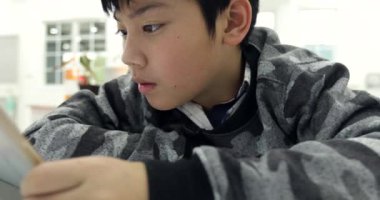 Asya yakışıklı genç genç çocuk gülümsemek yüz ile dijital tablet oyun oynamayı, tablet bilgisayar kullanarak .