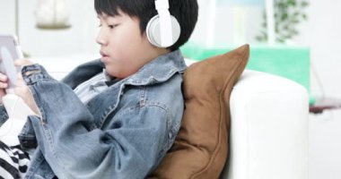 Genç Asyalı çocuk evde kulaklık ile tablet bilgisayarda oynama