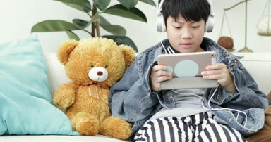 Genç Asyalı çocuk evde kulaklık ile tablet bilgisayarda oynama