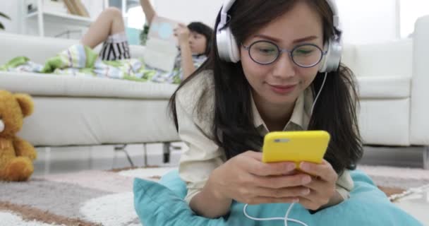 若いアジア女性リラックスできるリビング ルームでタブレット コンピューターで遊ぶ少年と音楽を聴く — ストック動画