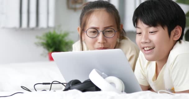 彼の妹と笑顔を自宅でラップトップ コンピューターを使用してベッドの上のかわいいアジアのプレティーンの少年残り — ストック動画