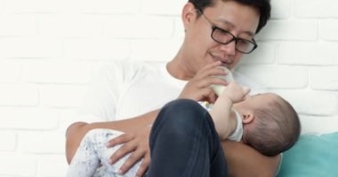 Genç Asyalı baba kız bebek besleme formül oturma odasında bir şişe süt