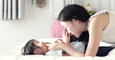 Genç Asyalı Anne ve yatağa birlikte, annelik güzel mutlu aile dinlenme öpüşme ve sarılma, çocuk. Genç annenin bebeği ile oynamak.