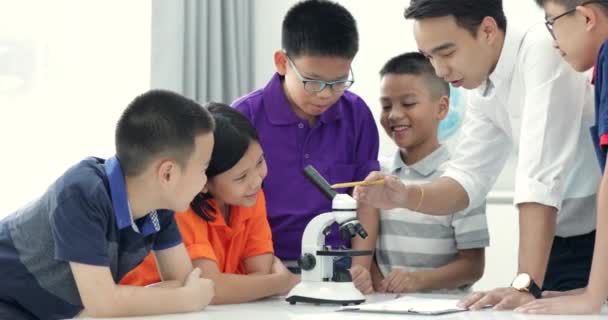 顕微鏡による生物学のクラスの学生に拡大アジアの教師 — ストック動画