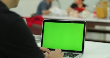 Bir anahtar yeşil ekran bilgisayarla çalışma grubu önünde set üzerinde bir dizüstü bilgisayarda yazarak bir Asya adam omuz çekim.