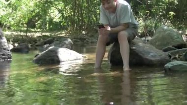 Tropikal bir ormanda tatildeyken cep telefonuyla konuşan Asyalı bir ergen..