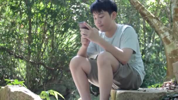 Azjatycki Nastolatek Typu Telefon Komórkowy Podczas Wakacji Tropikalnym Lesie — Wideo stockowe