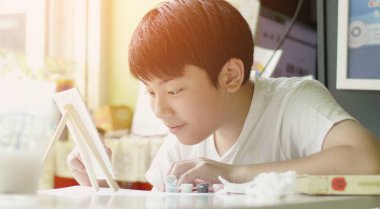 Genç Asyalı çocuk gülümseyen yüzüyle evi sulu boyuyor.,