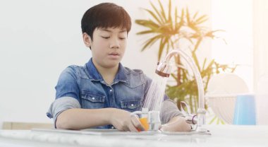 Asyalı genç çocuk mutfakta bulaşık yıkıyor..