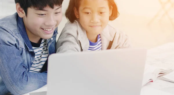 Mladý asijský chlapec a dívka hrát s notebookem doma. — Stock fotografie