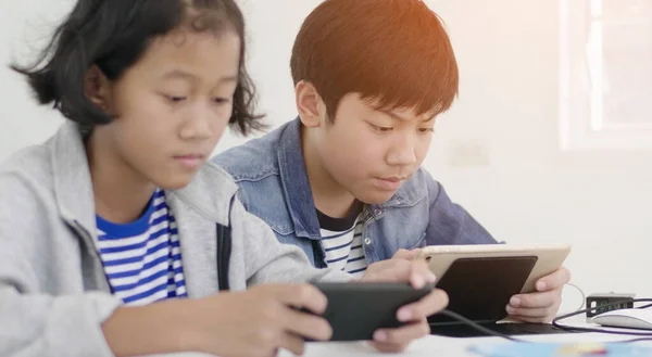 Menino e menina brincando com telefone inteligente e tablet computador em casa Fotografias De Stock Royalty-Free