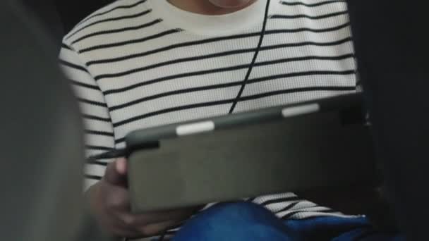 亚洲男孩开车旅行 带耳机的男孩在车上玩平板电脑和智能手机 — 图库视频影像