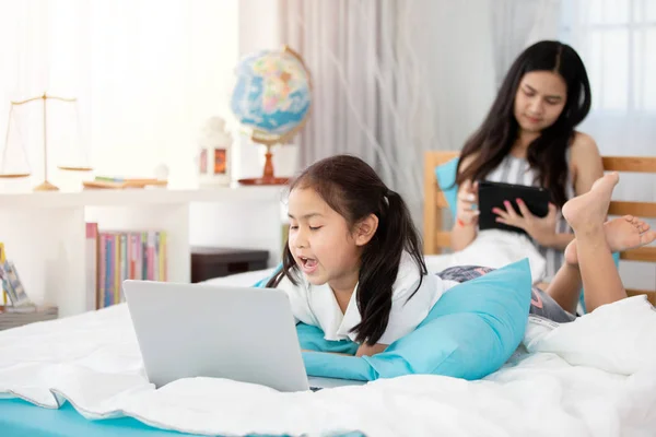 Két aranyos ázsiai gyerek lányok segítségével tabletta és laptop az ágyban. — Stock Fotó