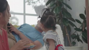 Kızı pastanın tadını çıkarıyor ve kendi evinde oturma odasında onunla oynuyor. Genç bir anne çocuğunun kek yemesine yardım eder. Ne mutlu.