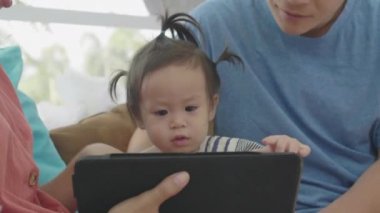 Asyalı ebeveynler tablet bilgisayar kullanıyorlar. Kızına bir şeyler öğretmek için. Teknolojiyi evde dikkatli bir şekilde yararlanmak için kullanarak..