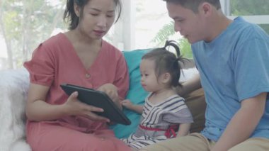 Asyalı ebeveynler tablet bilgisayar kullanıyorlar. Kızına bir şeyler öğretmek için. Teknolojiyi evde dikkatli bir şekilde yararlanmak için kullanarak..