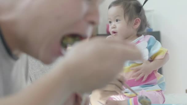 亚洲父母高高兴兴地在他自己家里的餐桌边给小女儿的午餐喂食 家庭欢乐时光 — 图库视频影像