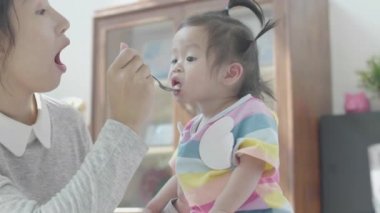 Asyalı ebeveynler kendi evindeki yemek masasında kızına yemek yediriyorlar. Aile mutlu anları.