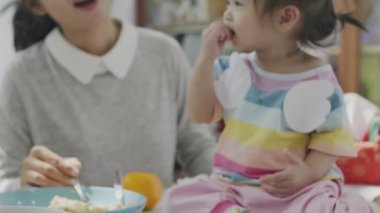 Asyalı ebeveynler kendi evindeki yemek masasında kızına yemek yediriyorlar. Aile mutlu anları.