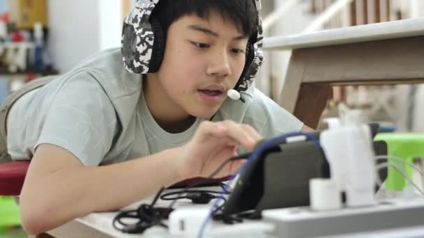 アジアの少年タブレットコンピュータで友人とオンラインゲームをプレイ 若い男性は興奮してマイクでヘッドフォンを通して話しています — ストック動画