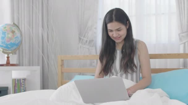 若いですアジアの女性使用してノートパソコンで笑顔でベッドに家 — ストック動画
