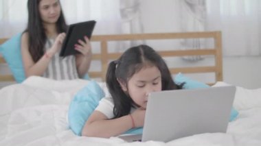 Asyalı kızlar ve kız kardeşler sanal dünyaya bağlanmak için dizüstü bilgisayarlar, bilgisayarlar ve tabletler kullanıyorlar. Küçük kız internet kullanarak evde dinlendi..