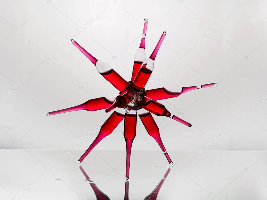 Glass ampoules with a red medicine vitamine b12 glued together in a spider shape on a glass laboratory shelf