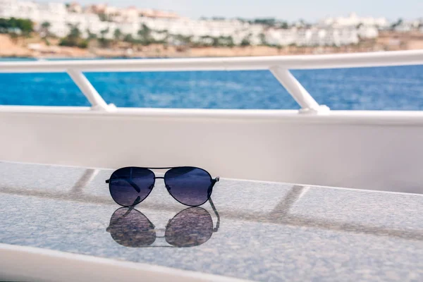 Bir tabloda deniz ve kıyı arka planı beyaz bir yatta güneş gözlüğü yalan