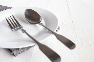 Gümüş çatal ve kaşık Beyaz ahşap masa üzerinde beyaz bir tabak.