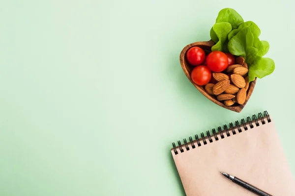 健康的な食事 新しい解像度の概念 薄緑色の背景に野菜やナッツとノートとハート型のプレート トップビュー フラットレイアウト コピースペース — ストック写真