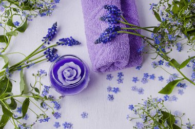 Beyaz ahşap arka planda mavi çiçekler, mumlar ve havlular için kaplıca kompozisyonu. Çiçek düzenlemesi 