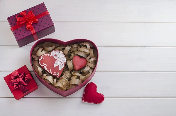 Sweets as a gift for Valentine\'s Day. Gingerbreads in the form of hearts with gifts with red ribbons with copy space on a white wooden background. Cooking